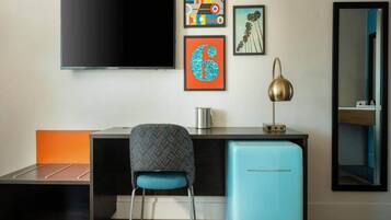Quarto moderno com televisão de tela plana, escrivaninha com cadeira, mini-geladeira e obras de arte nas paredes.