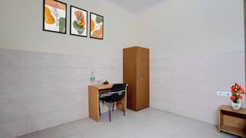 Una habitación con escritorio, silla, armario y una mesita con un jarrón de flores.