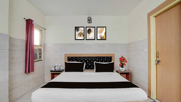Una habitación de hotel con cama, mesita de noche, ventana con cortina y tres cuadros en la pared.