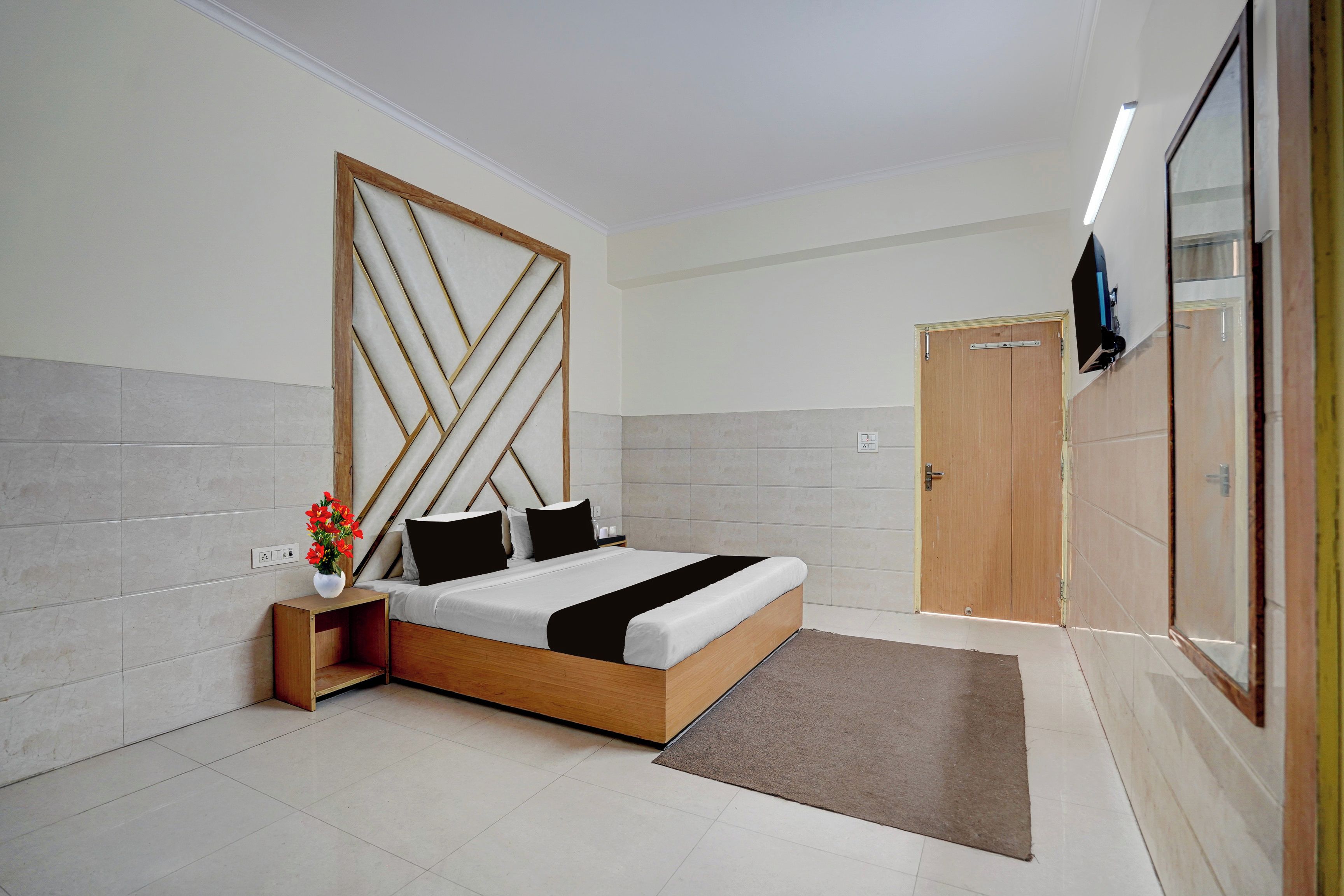 A modern bedroom with a wooden bed frame, a nightstand with a vase of flowers, and a wardrobe with a mirror.
