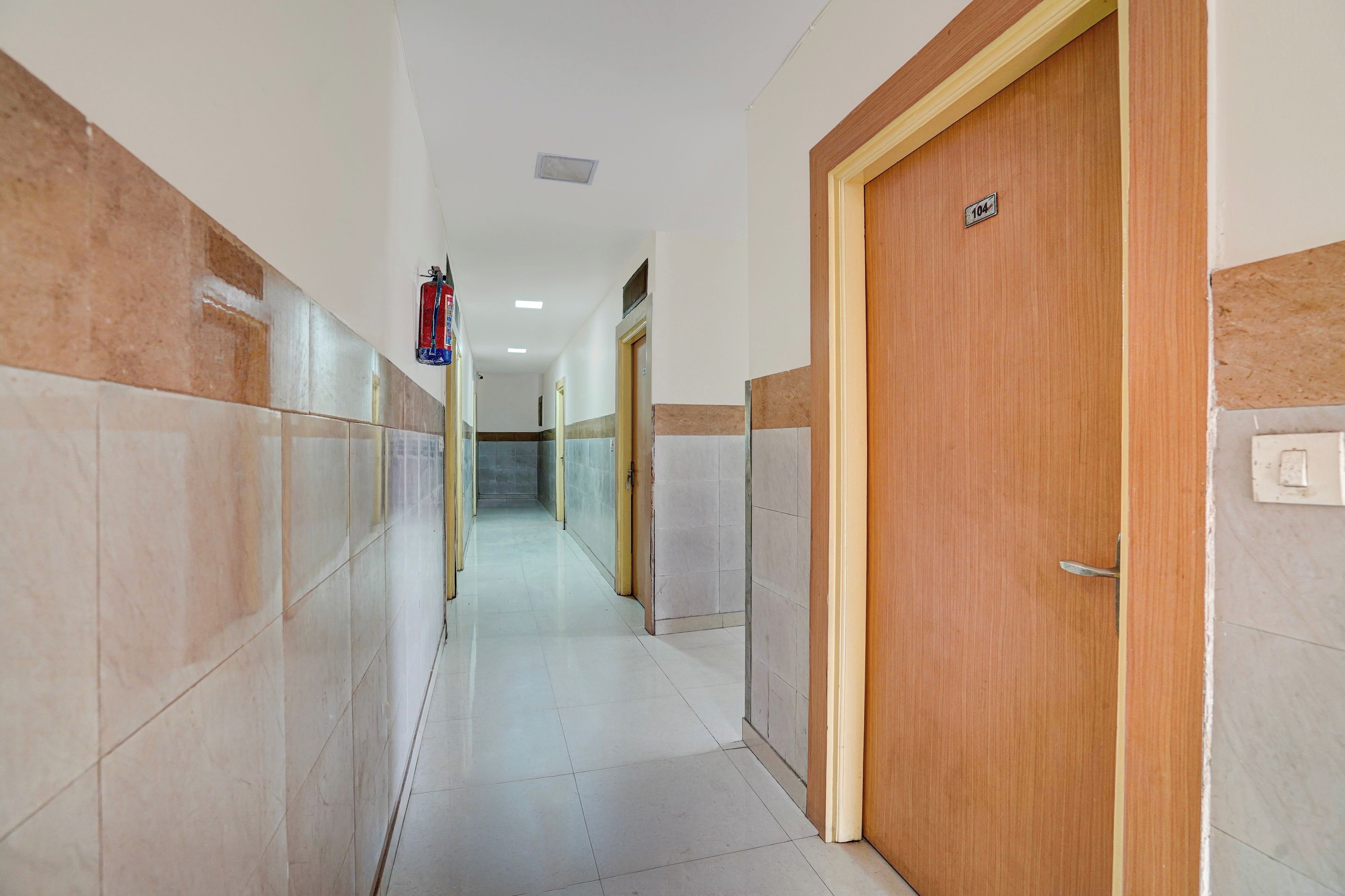 Un pasillo con paredes de azulejos, una puerta de madera con un número y un extintor.