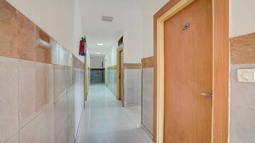 Un pasillo con paredes de azulejos, una puerta de madera con un número y un extintor.