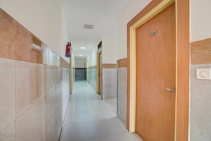 A corridor with tiled walls, a wooden door with a number, and a fire extinguisher. - Hotel O Sector 63 Noida FormerlyDaya Inn (Noida)