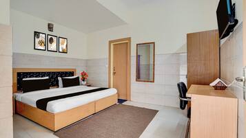 A hotel room with a bed, a desk, a chair, a mirror, and a television.