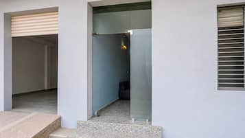 Entrada de un edificio moderno con puerta de vidrio, unos pocos escalones y un sofá de color oscuro en el interior.