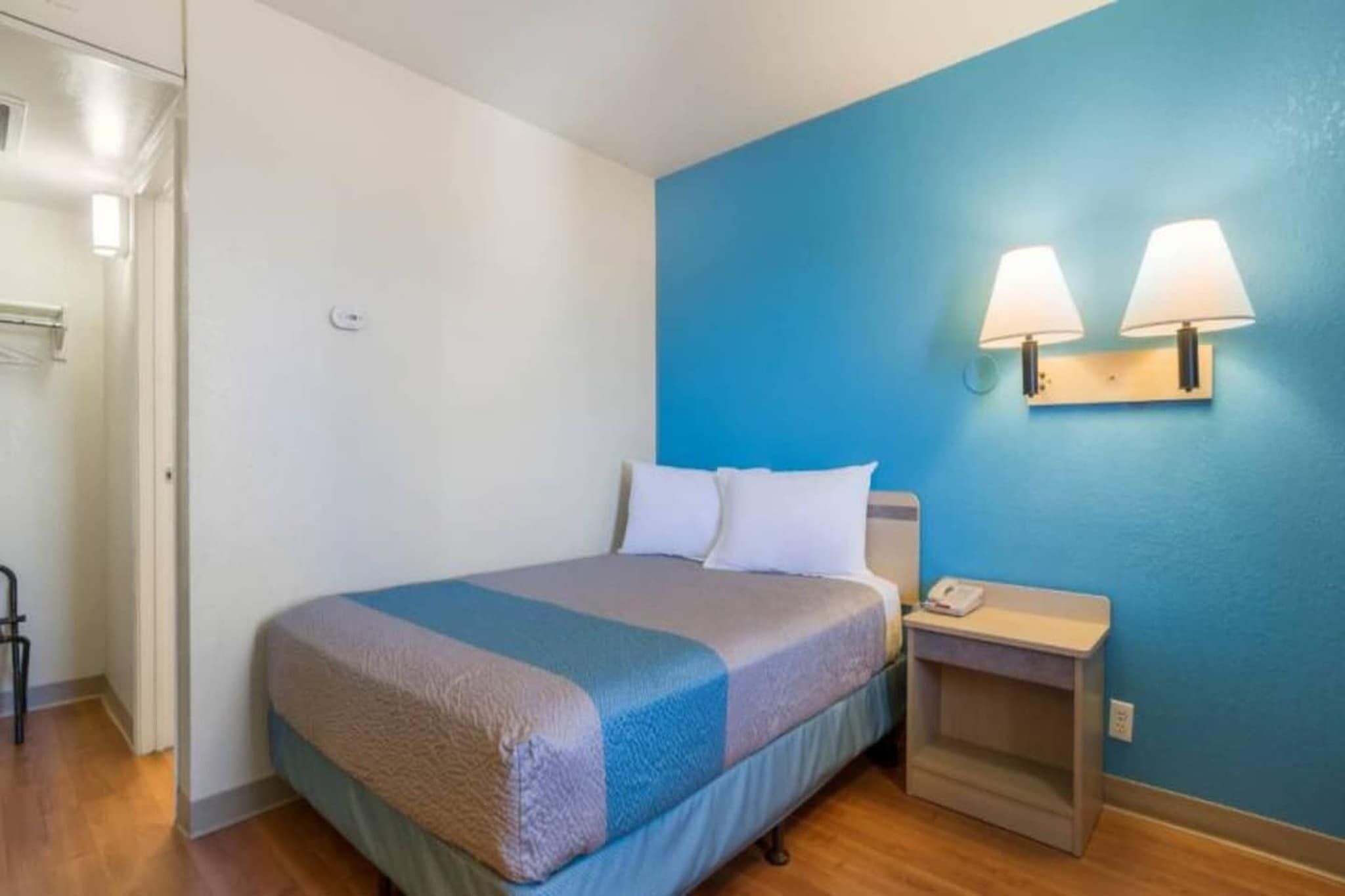 A hotel room with a bed, a nightstand, a lamp, and a blue wall.