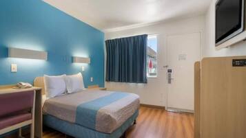 Habitación de hotel con cama, mesita de noche y televisor.