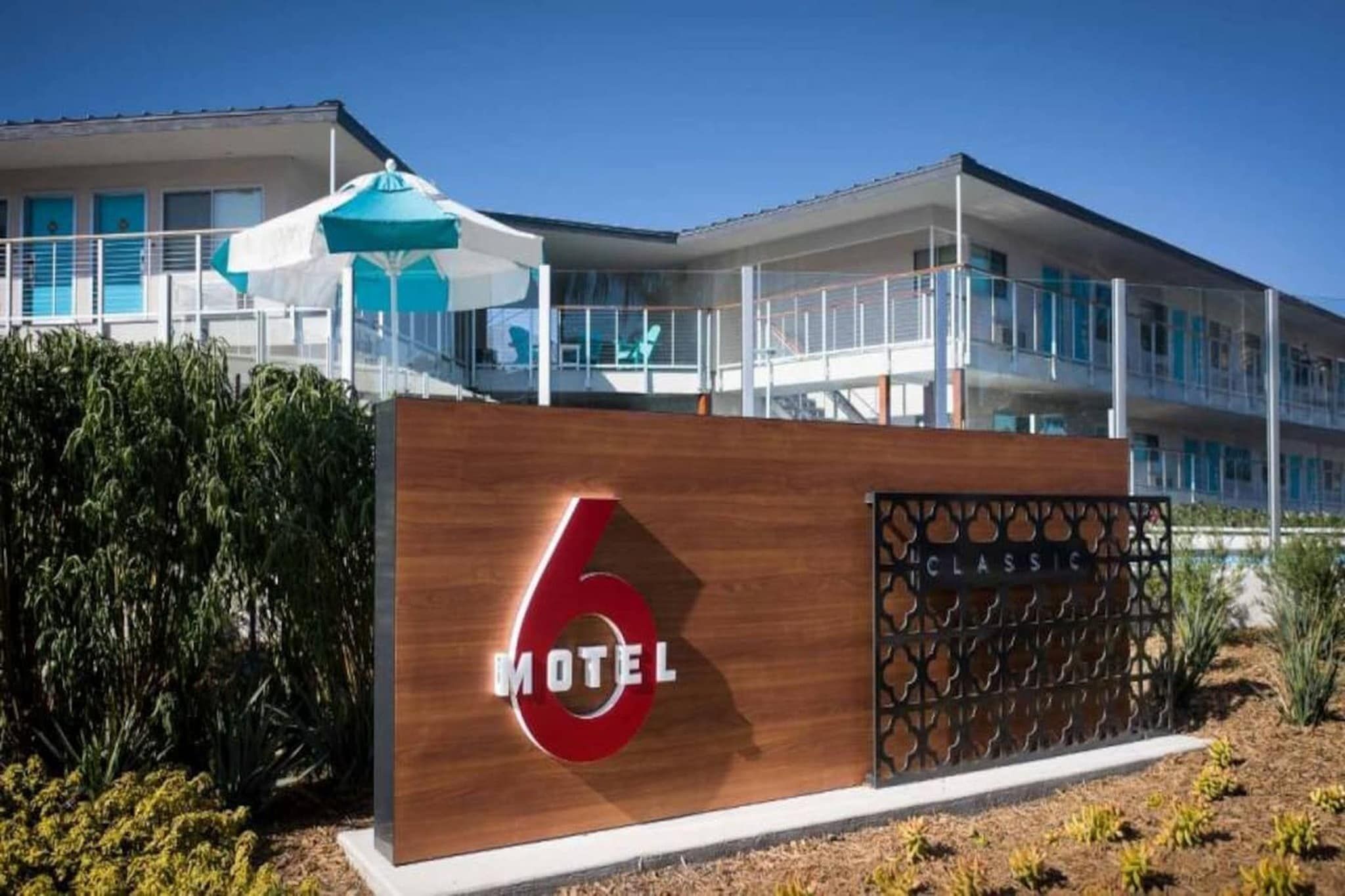 A modern motel with a prominent '6' sign, a covered outdoor seating area, and a balcony.