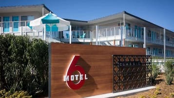 A modern motel with a prominent '6' sign, a covered outdoor seating area, and a balcony.