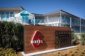 A modern motel with a prominent '6' sign, a covered outdoor seating area, and a balcony.