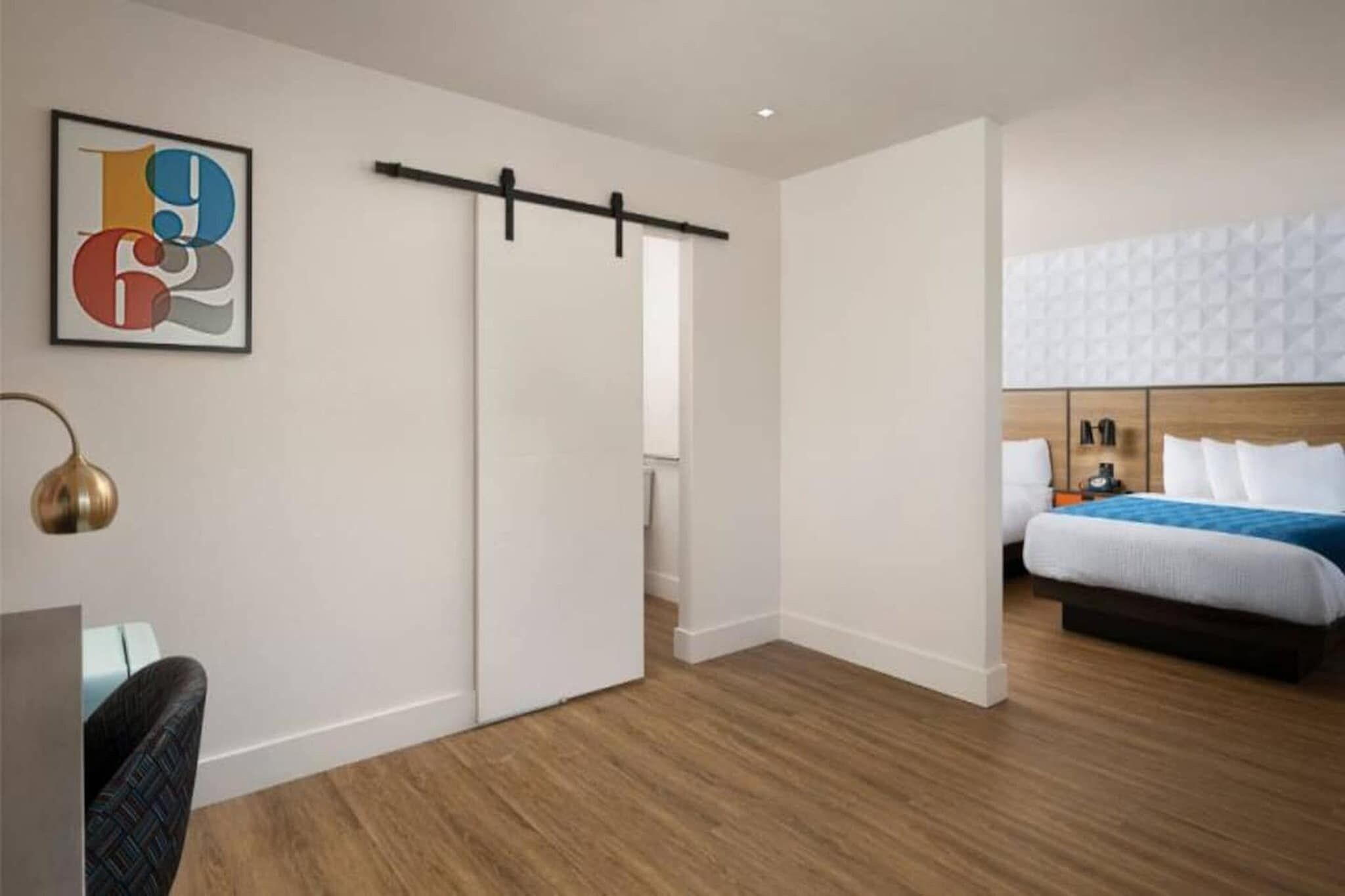 A hotel room with a bed, a desk, a chair, and a wall-mounted artwork.
