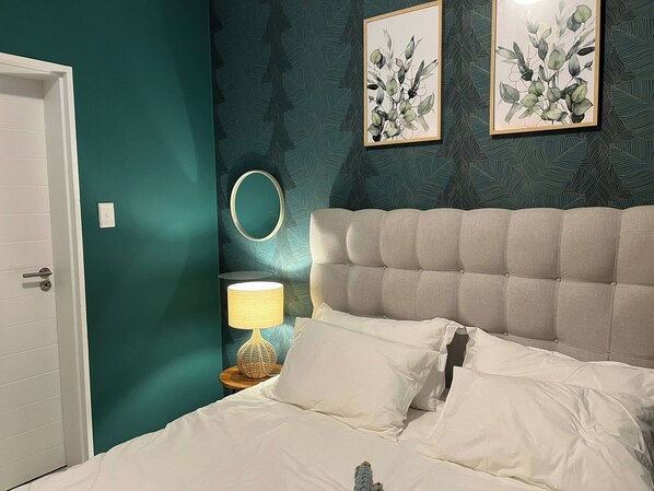 Ein Schlafzimmer mit türkisfarbenen Wänden, einem gesteppten Kopfteil, weißer Bettwäsche und zwei gerahmten Pflanzenbildern.