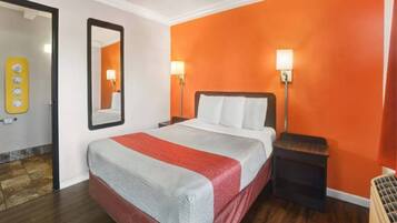 A hotel room with a bed, a nightstand, a mirror, and a wall with a light switch.