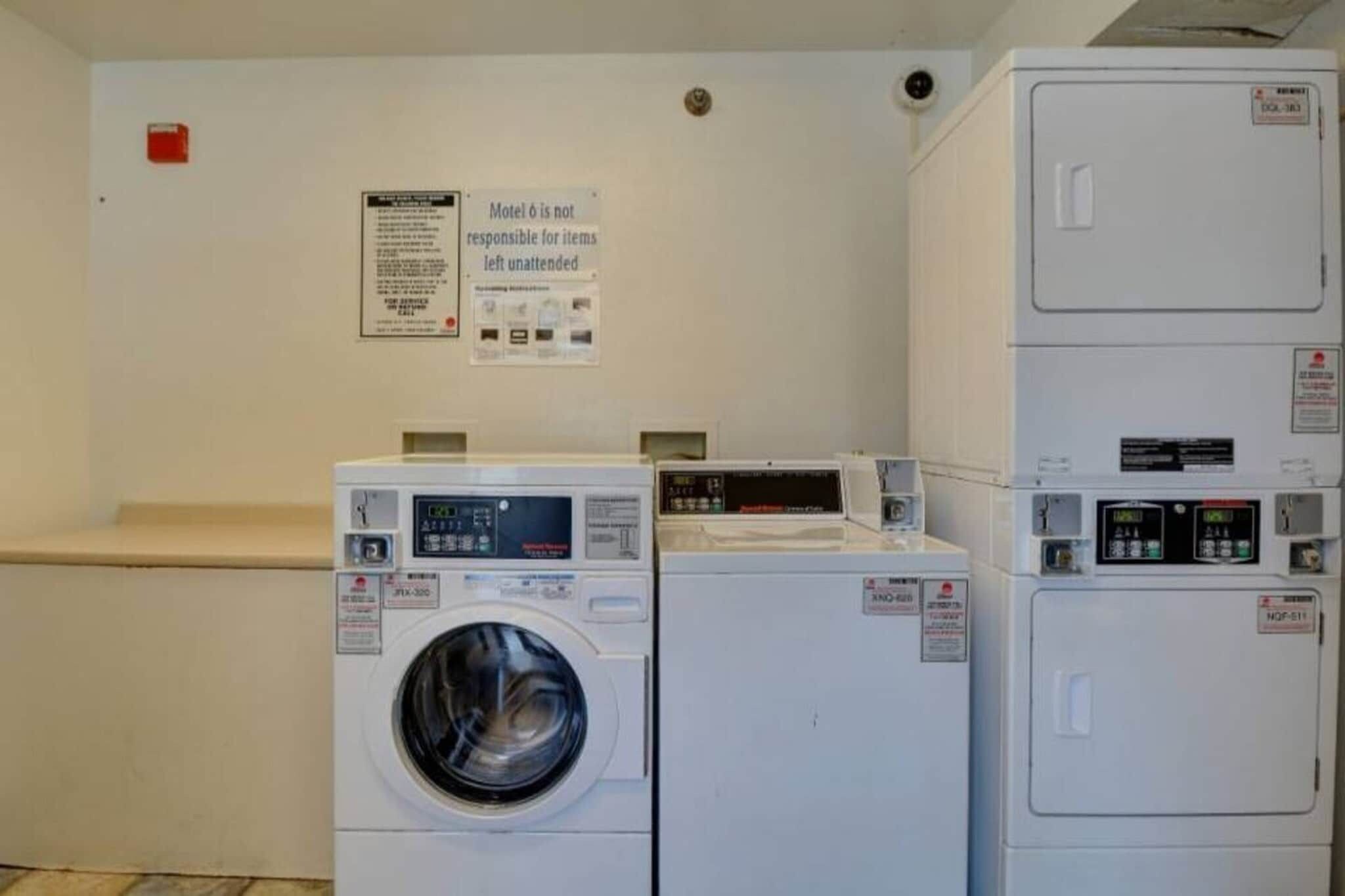 Zona de lavandería con lavadora, secadora y apilamiento de secadoras. Un cartel en la pared indica que el motel no se hace responsable por artículos desatendidos.