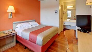 Una habitación de hotel con una cama, un escritorio, una silla, un televisor y un baño visible al fondo.