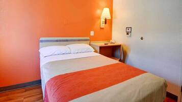 A hotel room with a bed, a nightstand, a lamp, and a wall-mounted phone.