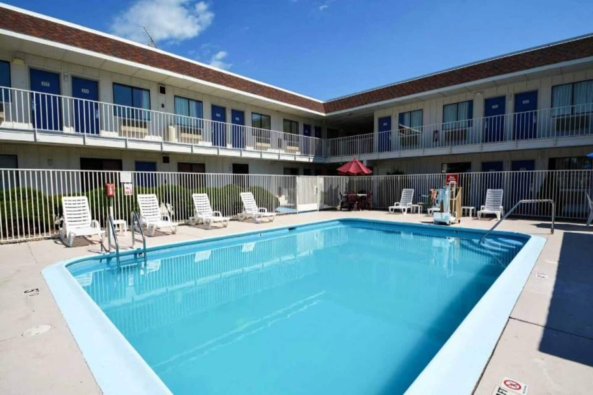 A swimming pool with lounge chairs and a fenced area, surrounded by a building with multiple balconies.