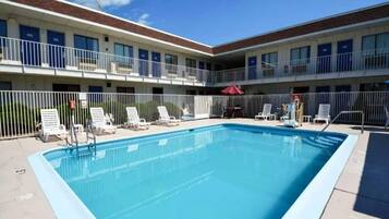 A swimming pool with lounge chairs and a fenced area, surrounded by a building with multiple balconies.