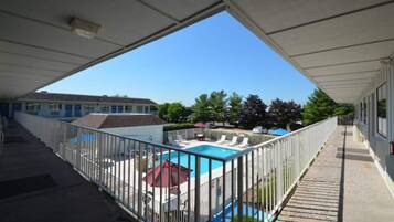 A covered outdoor area with a swimming pool, a fenced deck, and a building in the background.