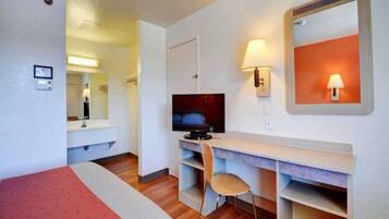 Een hotelkamer met een bed, een bureau, een televisie, een stoel en een spiegel.