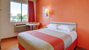 A hotel room with a bed, a desk, a window with curtains, and a wall-mounted lamp.