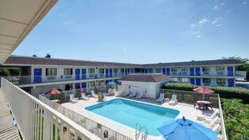 A hotel with a pool, multiple balconies, and a clear blue sky.