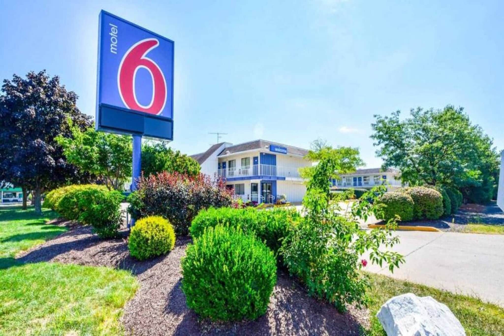 Un motel con un gran letrero con el número 6, un edificio de dos pisos y jardines bien cuidados.