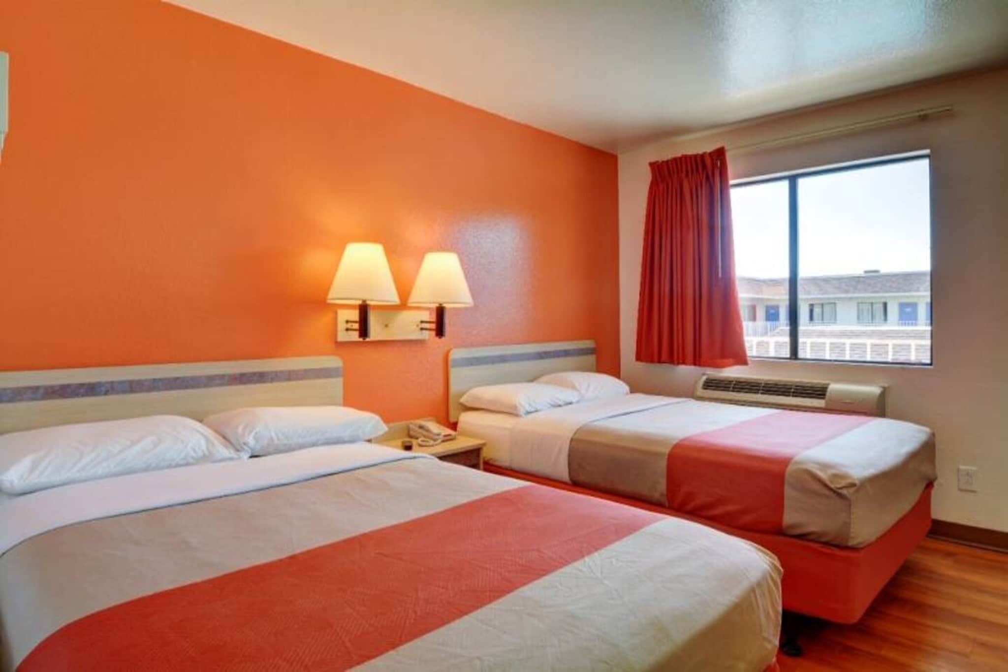 Una habitación de hotel con dos camas, un ventanal con vistas y una cortina roja.