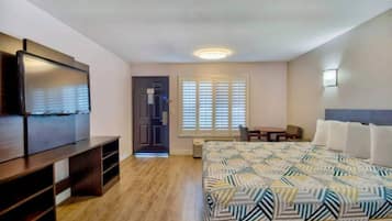 Een slaapkamer met een bed, een bureau, een stoel, een televisie en een raam met zonwering.