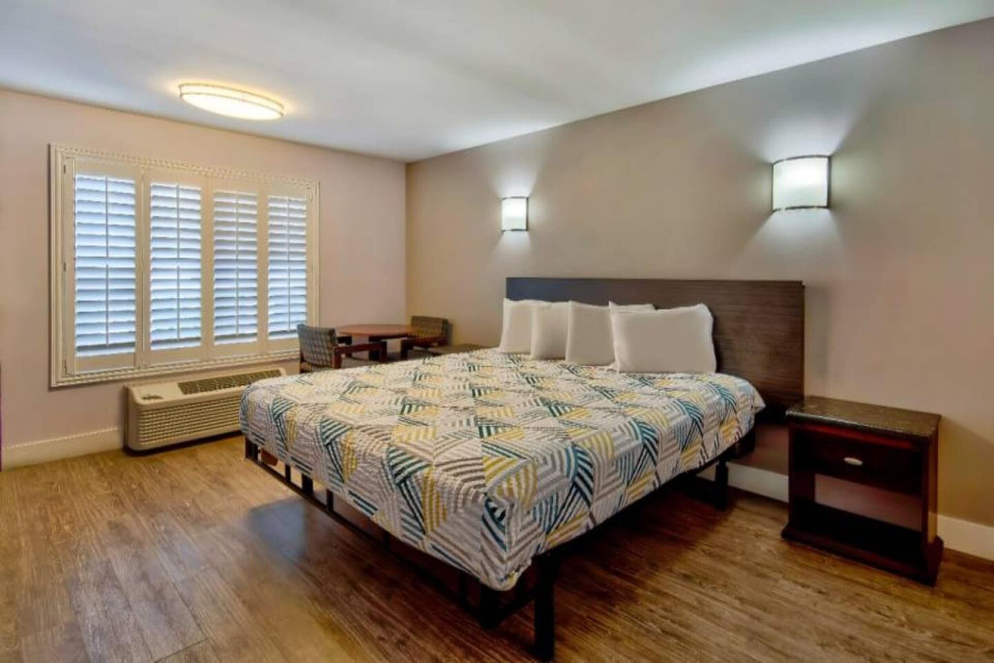 Een slaapkamer met een bed, nachtkastjes, een heater en een raam met jaloezieën.