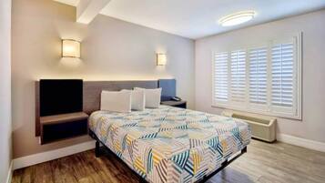 A bedroom with a bed, bedside tables, a wall-mounted TV, a window with blinds, and a built-in heater.