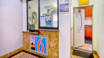 A hotel reception area with a marble counter, a large number '6' sign, and a door leading to a kitchen.