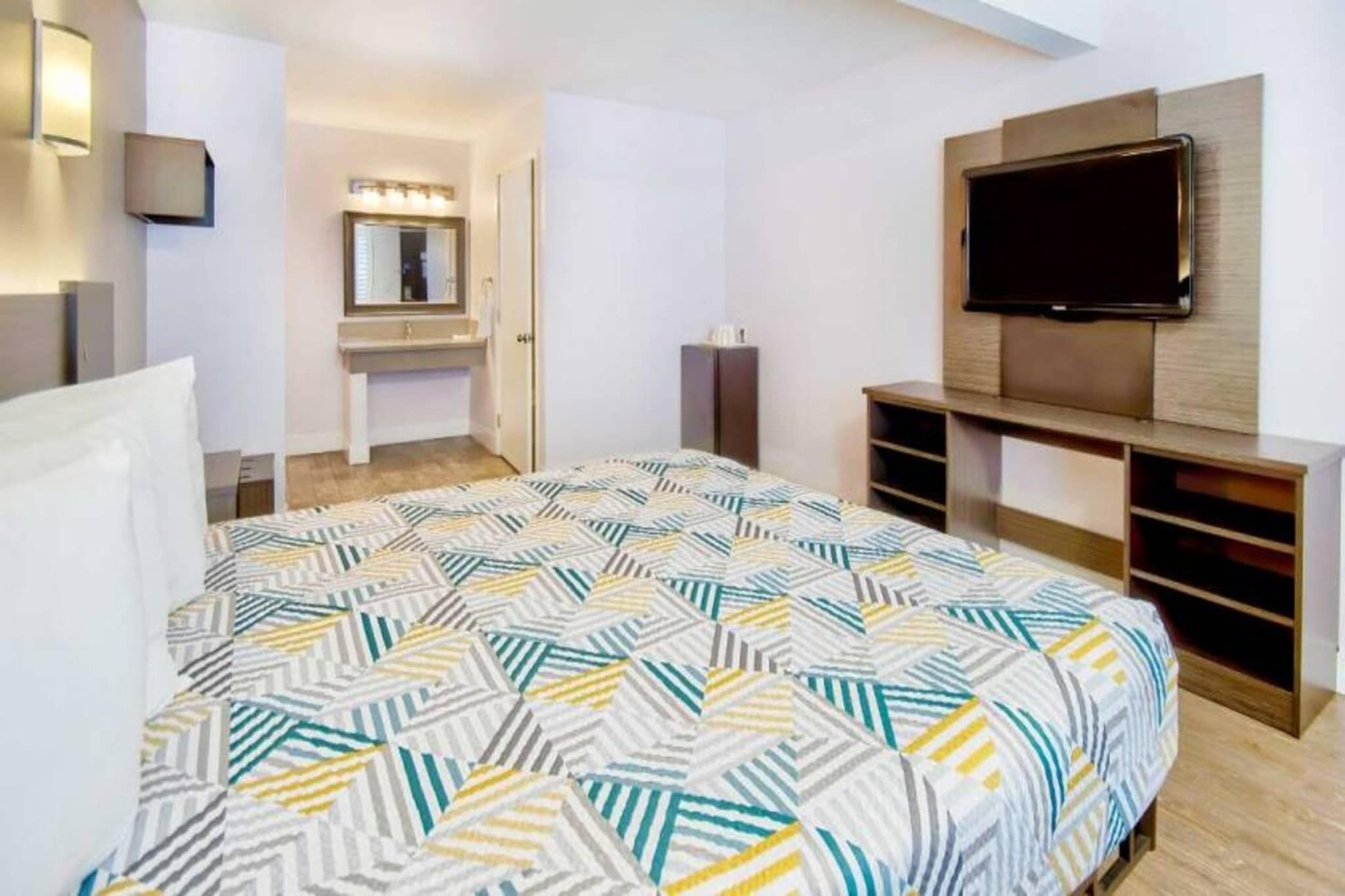 Een slaapkamer met een bed, een televisie, een spiegel en een kaptafel.