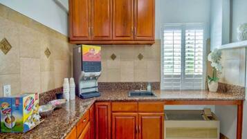 A kitchen with wooden cabinets, a coffee maker, and a window with blinds.