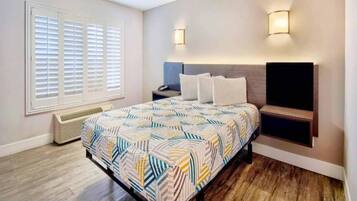 Une chambre à coucher comprenant un lit, des tables de chevet, un radiateur, un téléviseur et une fenêtre avec des stores.