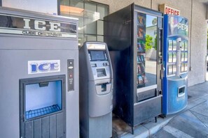 Trois distributeurs automatiques : l’un porte l’inscription « DISTRIBUTEUR DE GLAÇONS », et les deux autres affichent les mots « BUREAU » et « PEPSI ».