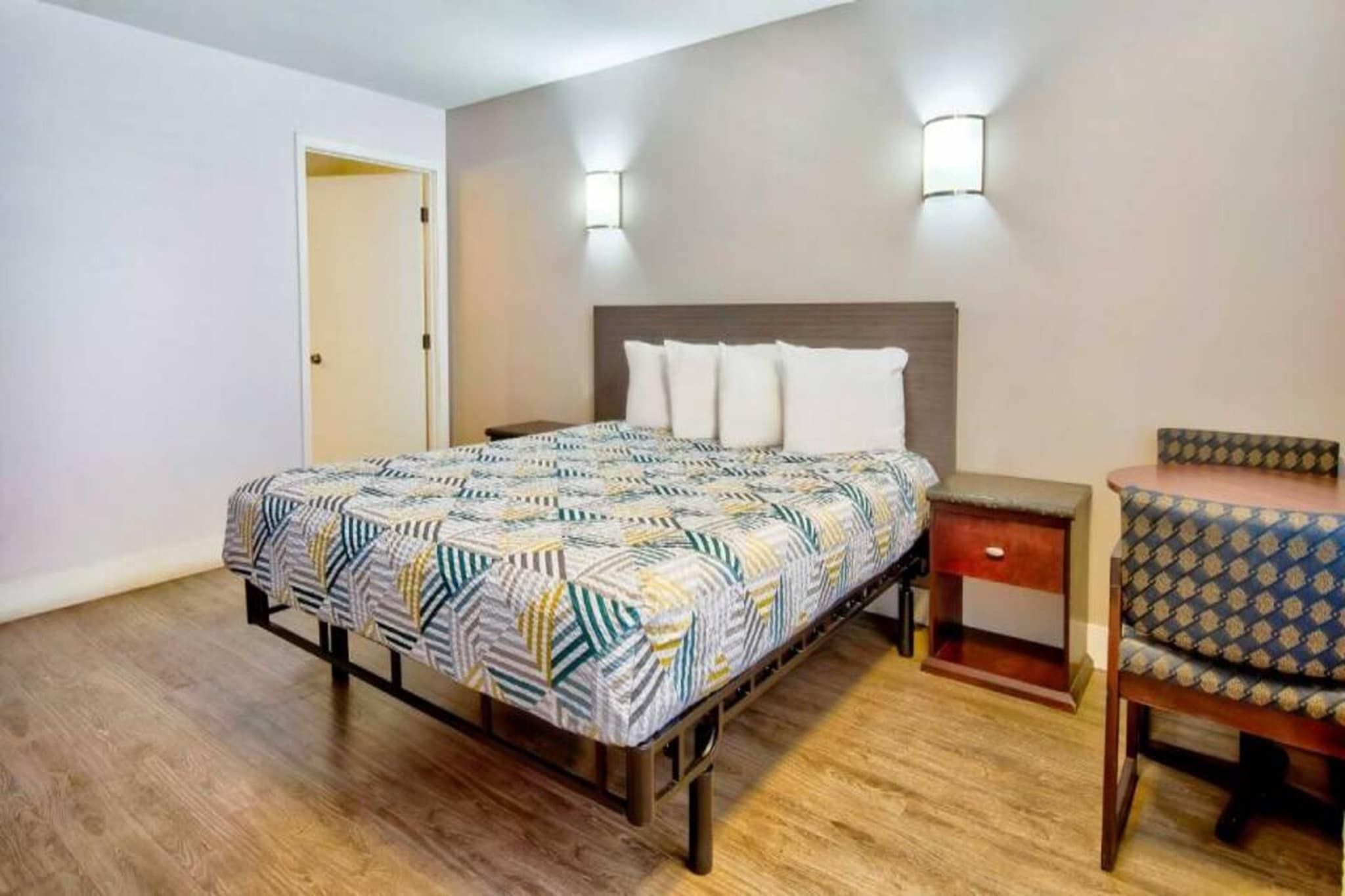 Een slaapkamer met een bed, nachtkastje, stoel en een deur.