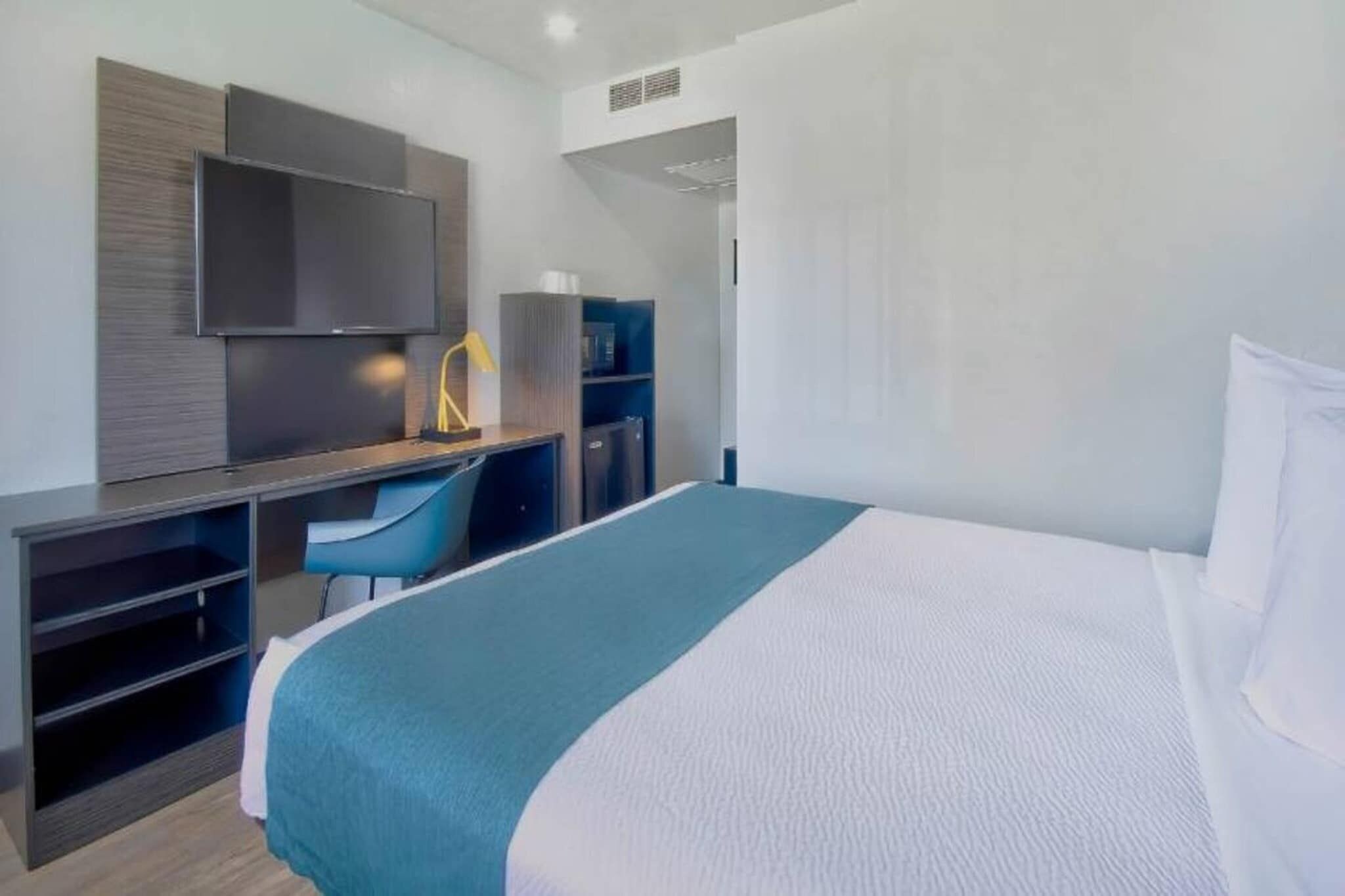 A hotel room with a bed, a desk, a chair, a television, and a wardrobe.