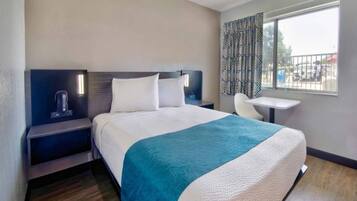 A hotel room with a bed, bedside tables, a chair, a small table, and a window with a view.