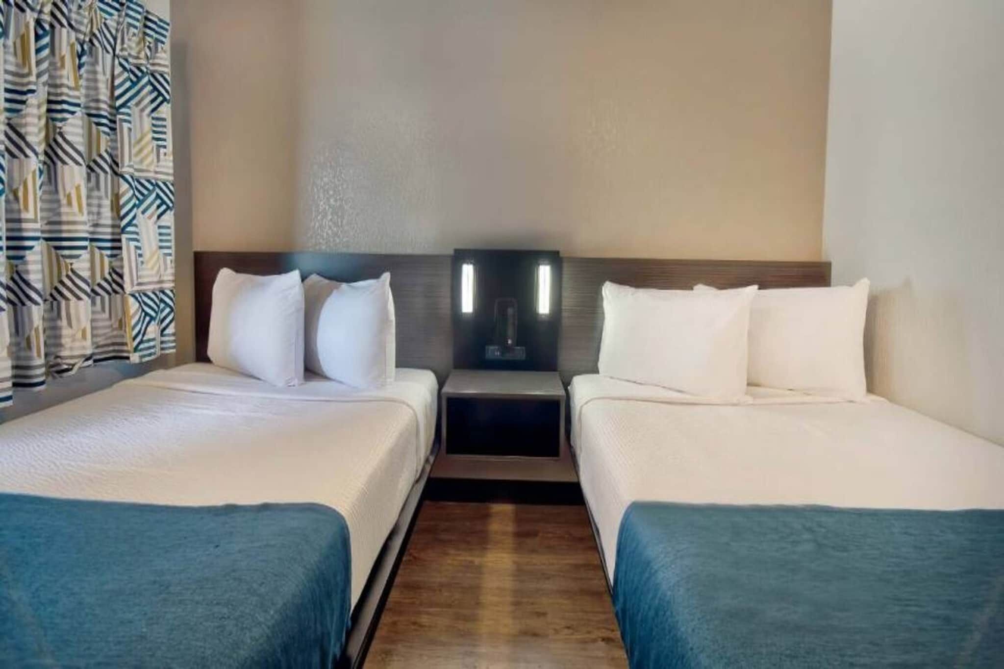 Ein Hotelzimmer mit zwei Betten, einem Nachttisch und einer wandmontierten Lampe.