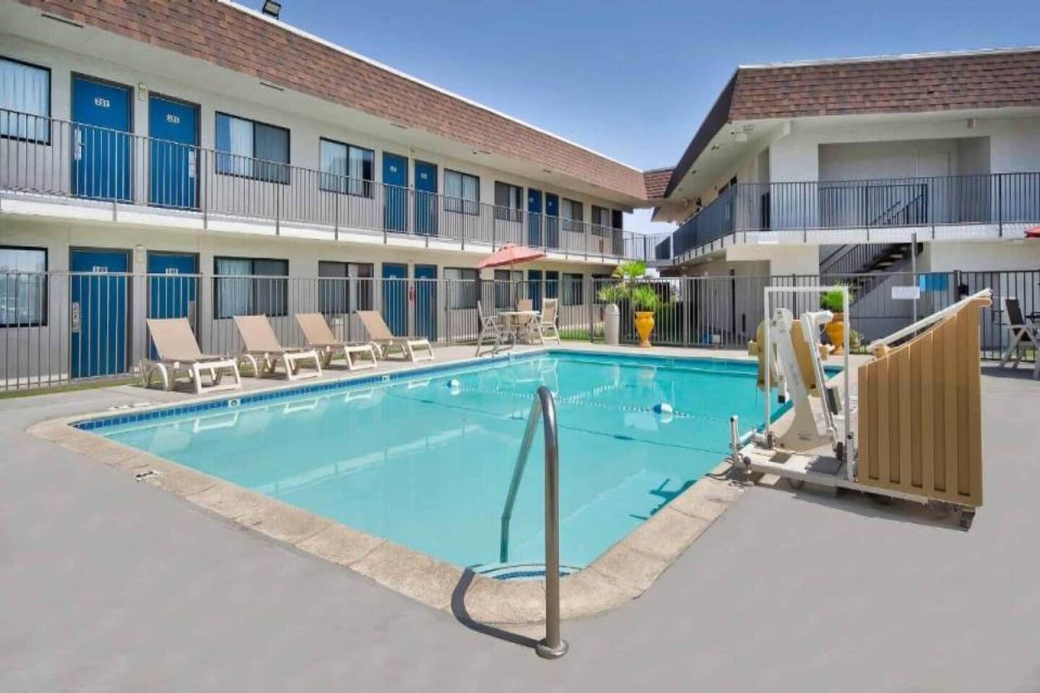 A swimming pool with lounge chairs and a building with multiple windows and doors.