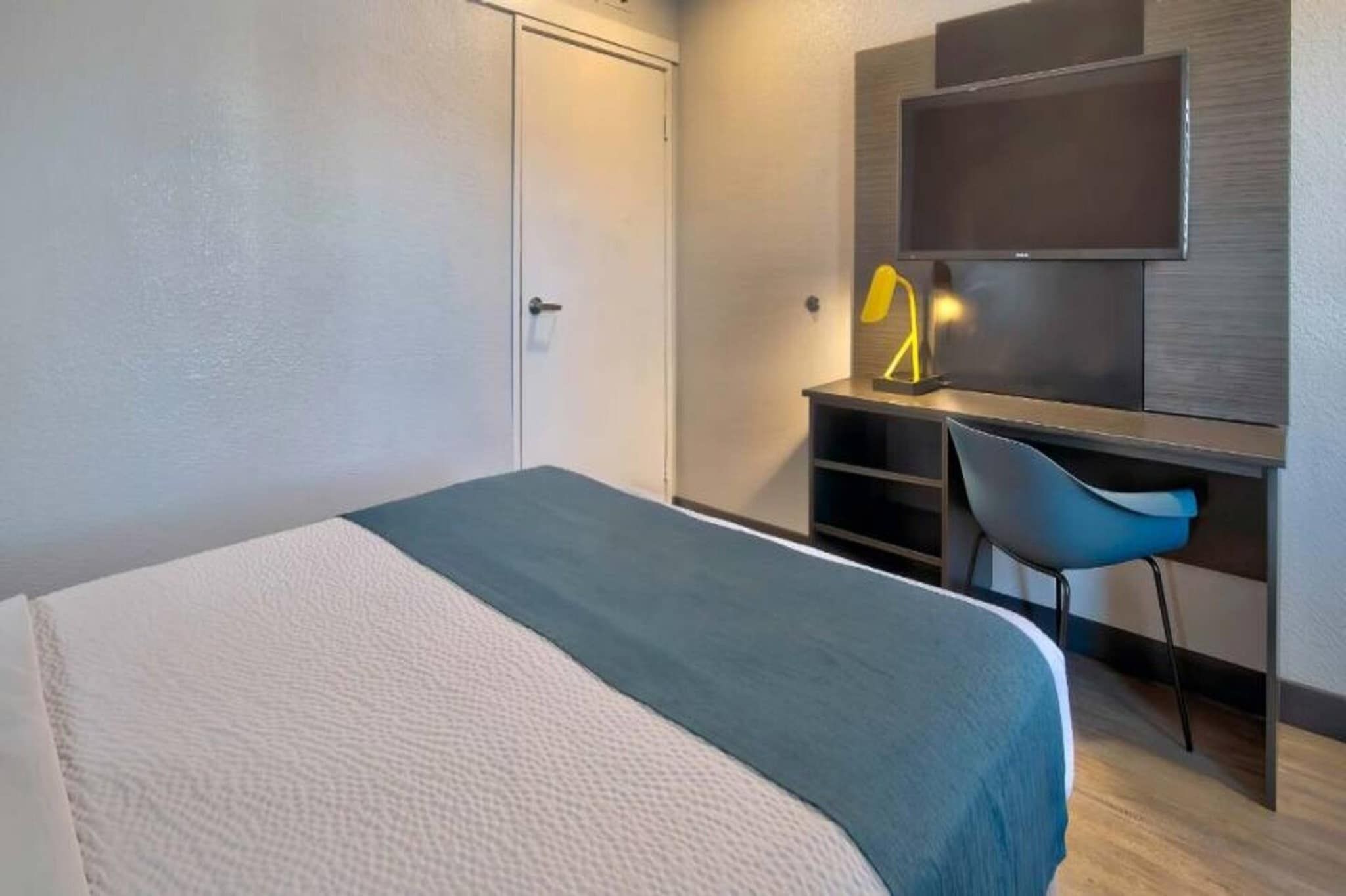 A hotel room with a bed, a desk, a chair, and a TV.
