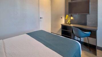 A hotel room with a bed, a desk, a chair, and a TV.