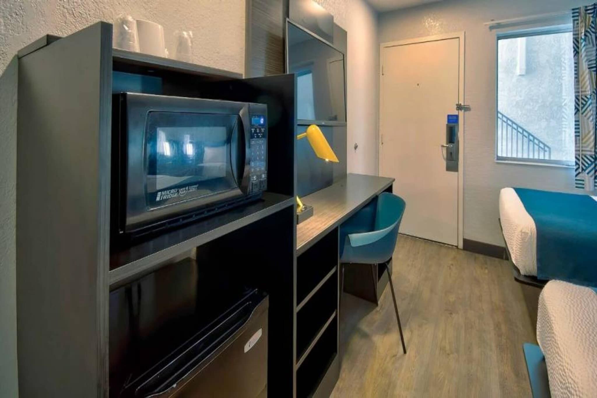 A compact room with a microwave, a desk, a chair, and a bed.
