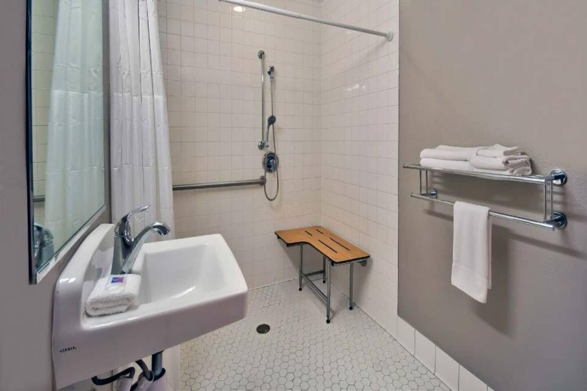 A bathroom with a sink, shower, and a small wooden stool.