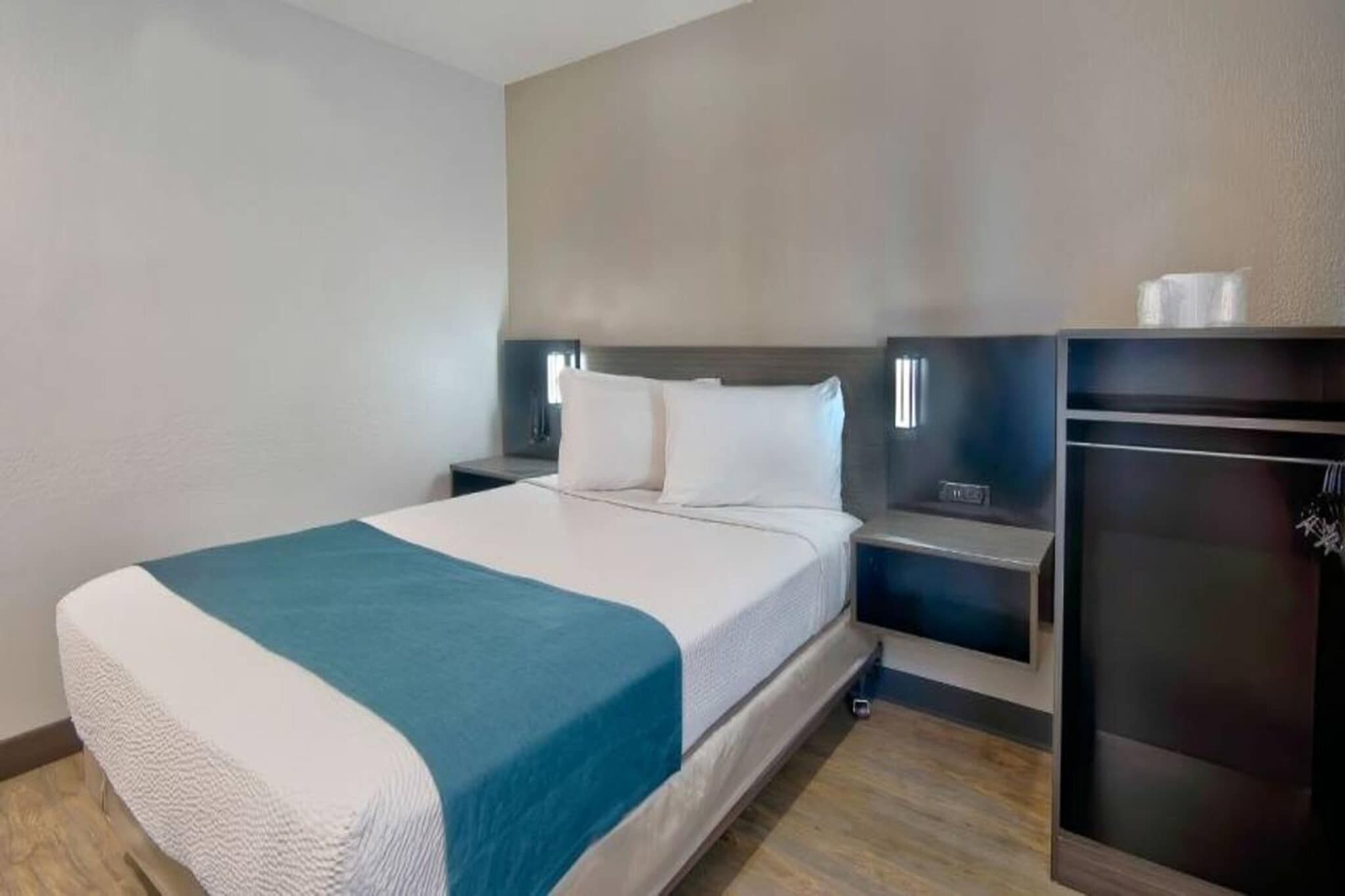 A hotel room with a bed, bedside tables, a TV, and a small kitchenette.