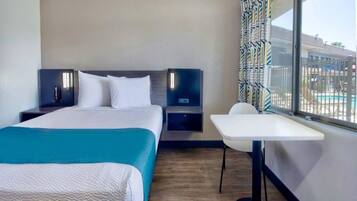 A hotel room with a bed, bedside tables, a desk, and a window with a view of a pool.