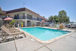 A swimming pool with lounge chairs and umbrellas, surrounded by a fenced area with a building in the background.
