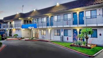 A motel with a 'Welcome' sign, multiple rooms, and a parking lot.