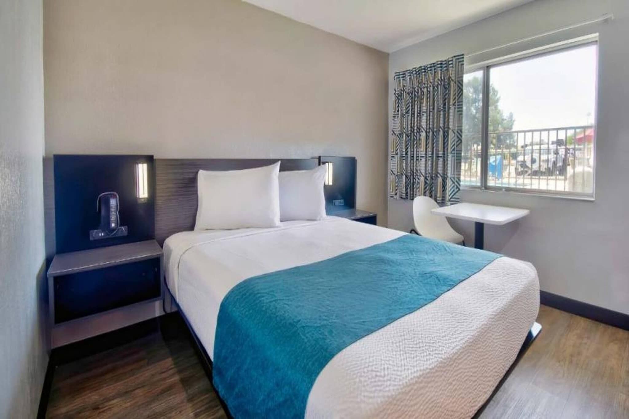 A hotel room with a bed, bedside tables, a chair, a small table, and a window with a view.